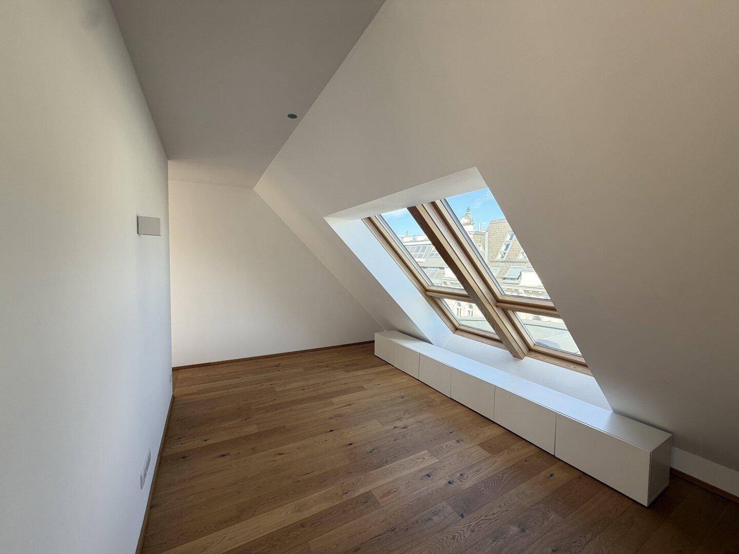 Geräumiges Dachzimmer mit schrägen Wänden, großen Dachfenstern und hellem Holzboden, bietet viel Tageslicht.
