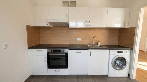 Moderne Einbauküche mit weißen Schränken, dunkler Arbeitsplatte und integrierten Geräten.