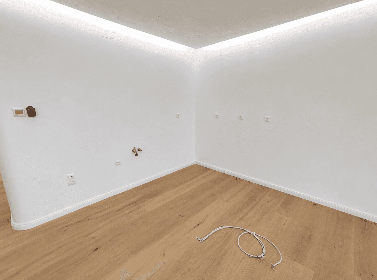 Leere Raumecke mit Holzboden und Anschlüssen, ideal für eine zukünftige Küche oder einen Hauswirtschaftsraum.