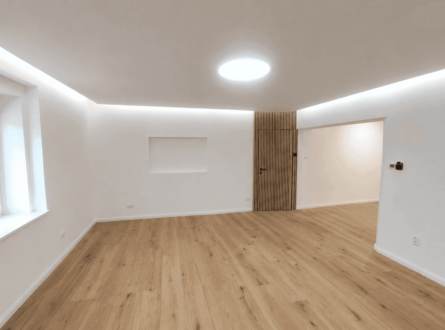Leerer Raum mit Holzboden, weiß gestrichenen Wänden und einer dekorativen Holzlamellenwand.