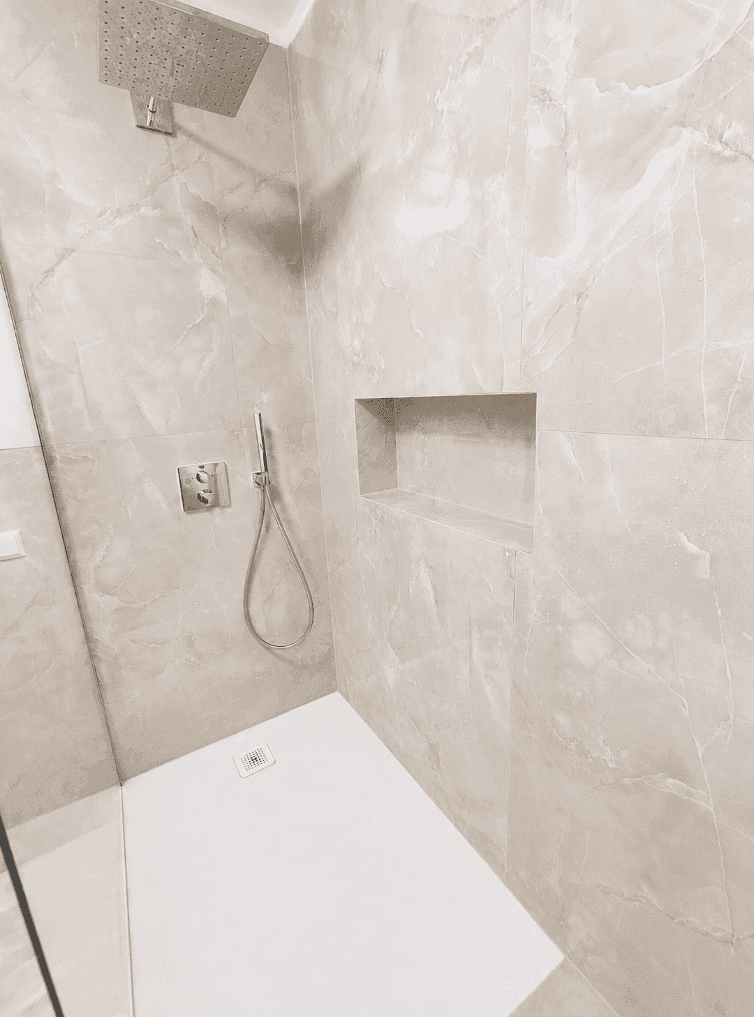 Detailaufnahme einer modernen Dusche mit Regenduschkopf und praktischer Ablagenische.