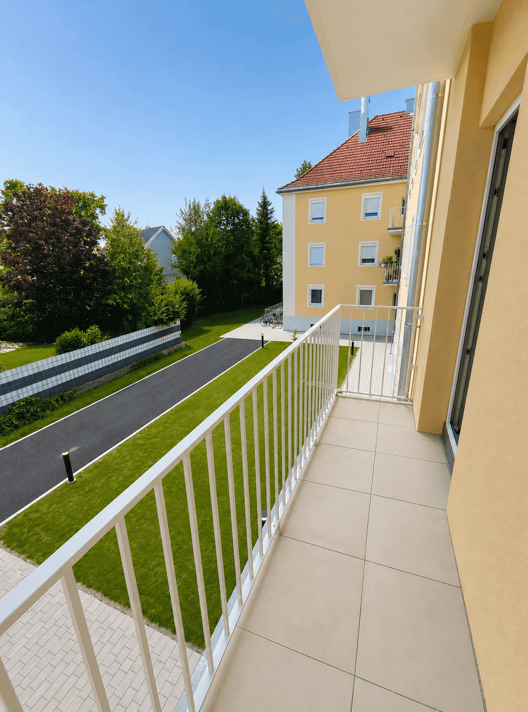 Heller Balkon mit Fliesenboden und weißem Geländer, bietet Blick auf die grüne Umgebung.