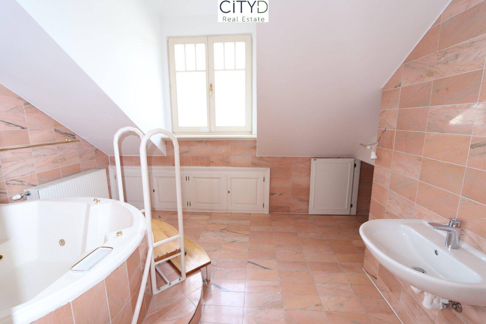 Geräumiges Badezimmer mit rosa Fliesen, Whirlpool-Badewanne, Einzelwaschbecken und Fenster.
