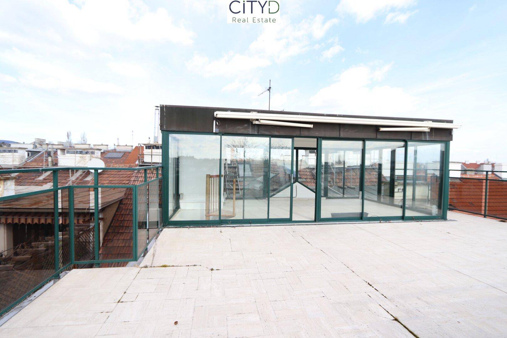 Weitläufige Dachterrasse mit einem verglasten Wintergarten und Panoramablick über die Stadt.