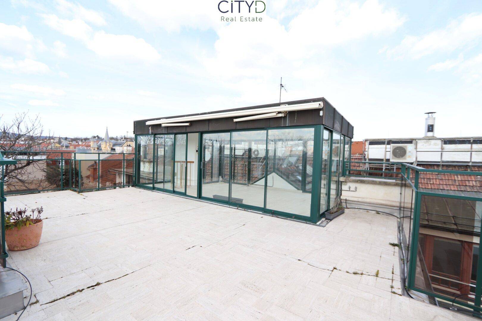 Weitläufige Dachterrasse mit einem verglasten Wintergarten und Panoramablick über die Stadt.