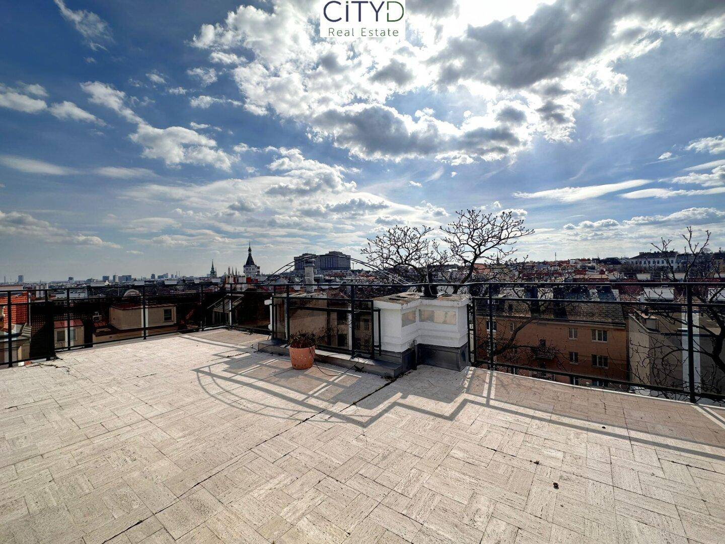 Weitläufige Dachterrasse mit Stadtblick, gefliestem Boden und einem kleinen gemauerten Grillbereich.