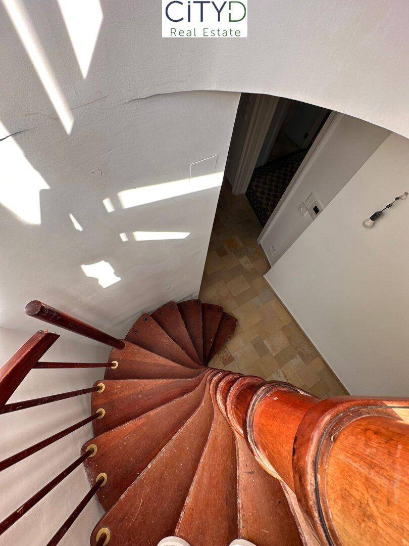 Elegante Holzwendeltreppe mit schmiedeeisernem Geländer, die verschiedene Ebenen des Hauses verbindet.