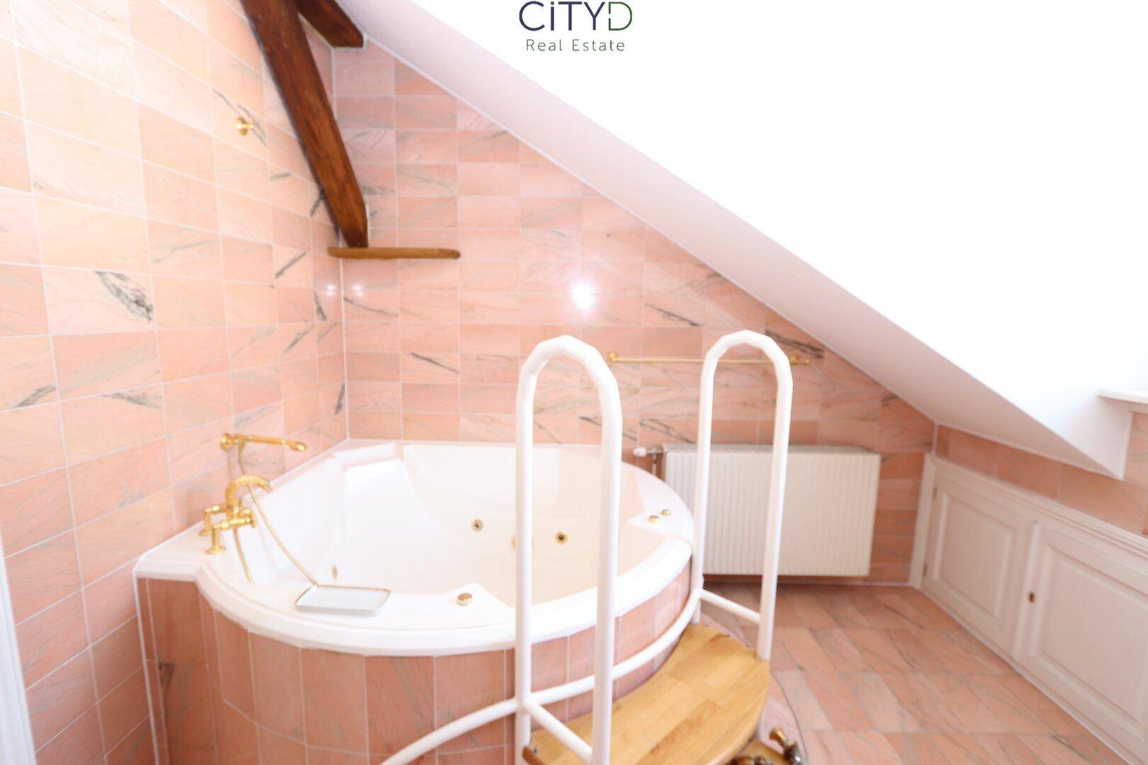 Badezimmer mit rosa Fliesen, Whirlpool-Badewanne und Dachschräge, die dem Raum Charakter verleiht.
