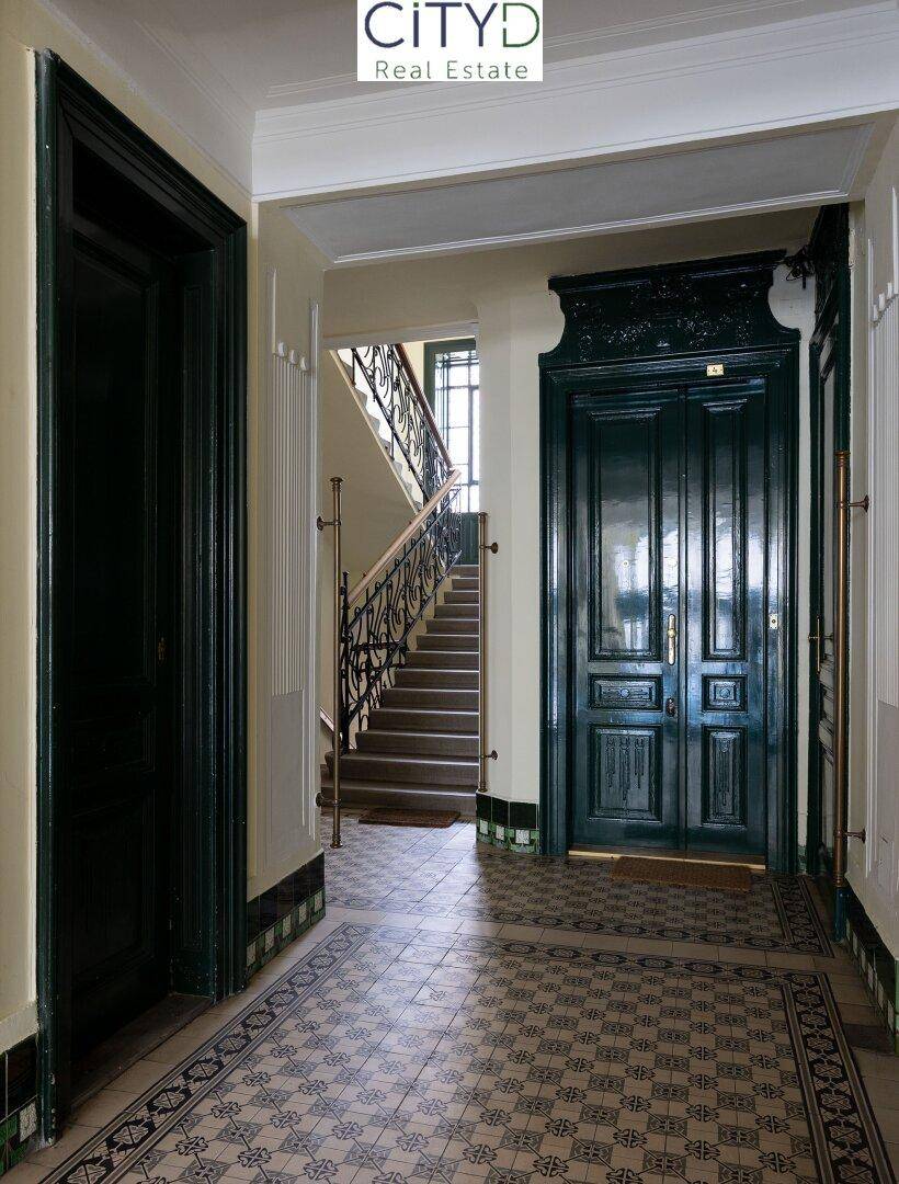 Historischer Eingangsbereich mit gemusterten Fliesen, hohen Decken und einer eleganten Treppe.