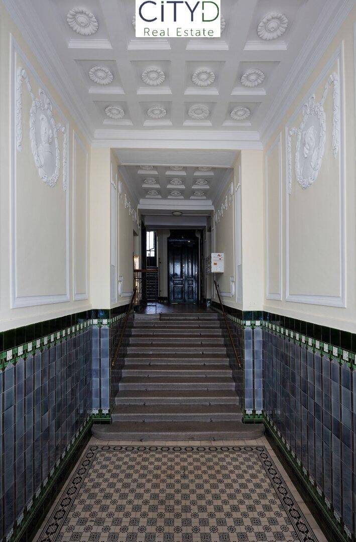Elegante Eingangshalle eines Altbaus mit hohen Decken, Stuckverzierungen und historischen Fliesen.