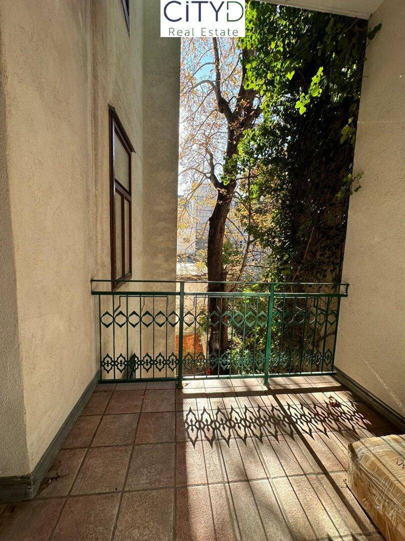Kleiner Balkon mit Fliesenboden und schmiedeeisernem Geländer, umgeben von Bäumen.