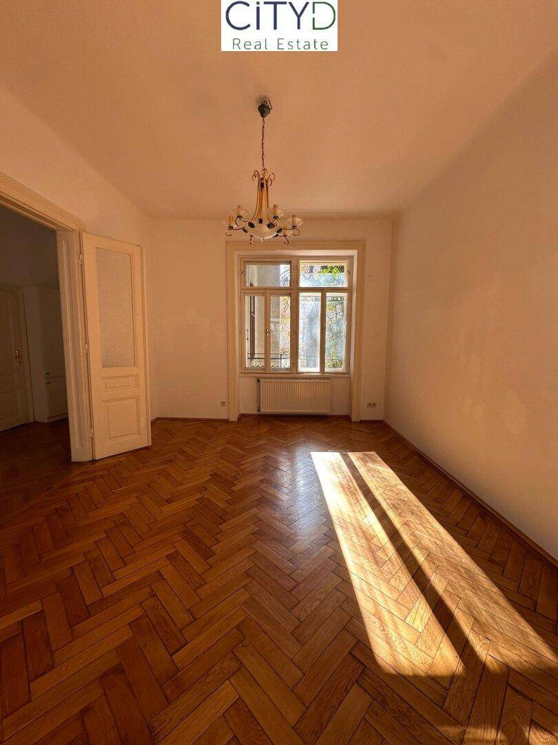 Lichtdurchflutetes Zimmer mit Fischgrätparkett und einem großen Fenster, das viel Sonne einfängt.