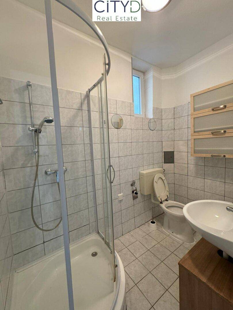 Gefliestes Badezimmer mit Dusche, WC und Waschbecken, ausgestattet mit einem Fenster.
