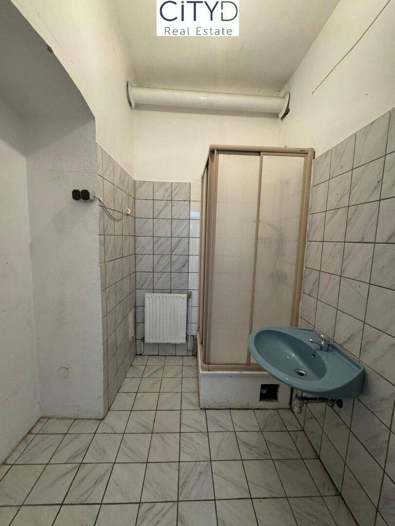 Einfaches Badezimmer mit Duschkabine, Waschbecken und gefliesten Wänden.