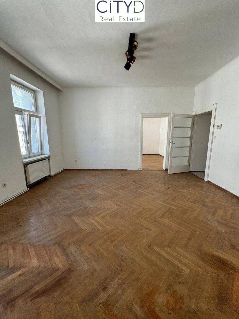 Großes Zimmer mit Fischgrätparkett und mehreren Türen, bietet vielseitige Nutzungsmöglichkeiten.