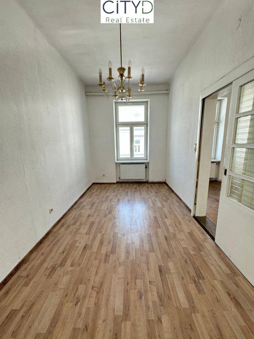 Langes Zimmer mit Laminatboden und Kronleuchter, bietet Platz für Schlaf- oder Arbeitsbereich.