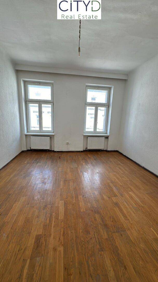 Geräumiges Zimmer mit Holzboden und zwei großen Fenstern, ideal für individuelle Gestaltung.