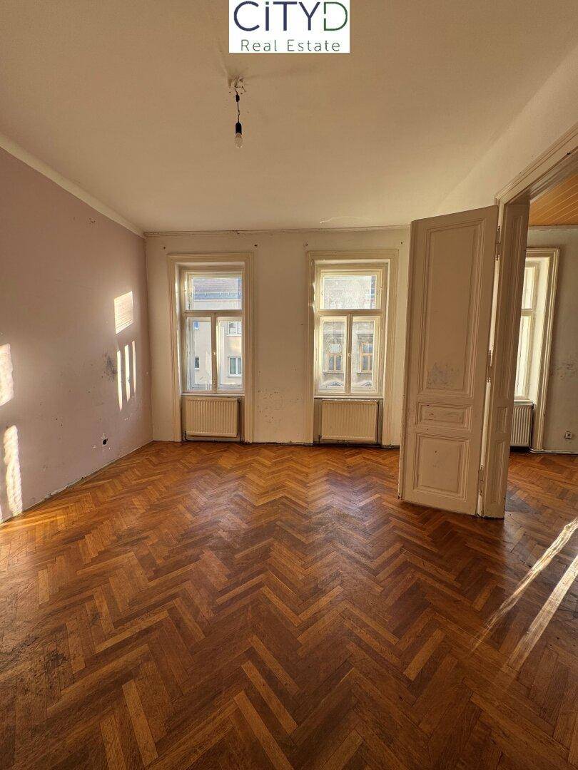Geräumiges Zimmer mit Fischgrätparkett und hohen Decken, ideal für eine Renovierung.