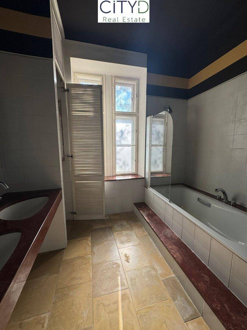 Badezimmer im 80er-Jahre-Stil mit Fliesenboden, Badewanne und Doppelwaschbecken.