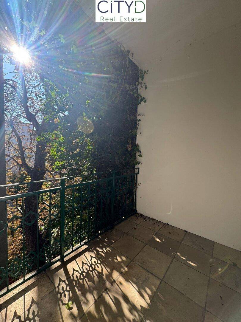 Sonniger Balkon mit schmiedeeisernem Geländer und Blick ins Grüne.