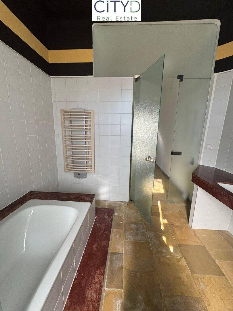 Badezimmer mit Badewanne, Duschbereich, beheiztem Handtuchhalter und Fliesenboden.