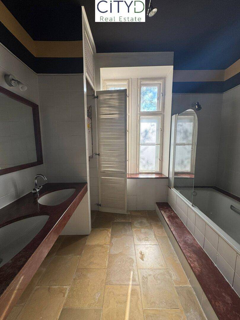 Badezimmer mit Fliesenboden, Badewanne, Doppelwaschbecken und Fenster für Tageslicht.