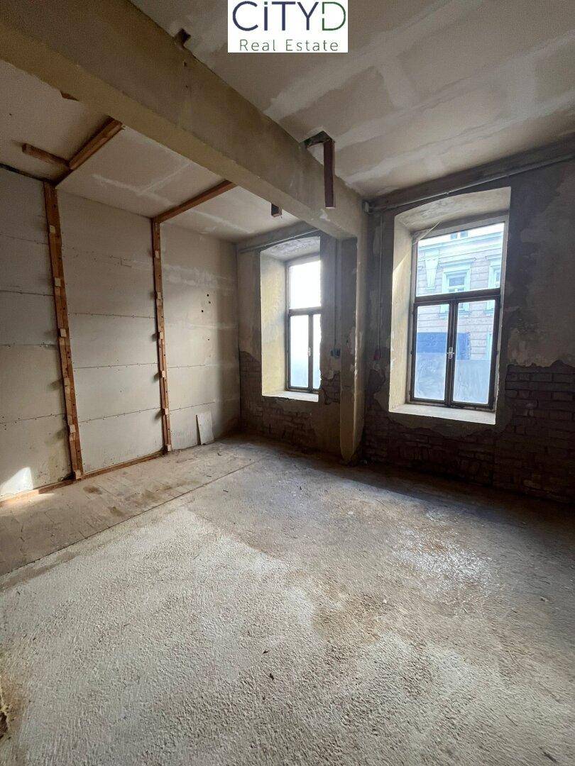 Rohbau-Innenraum mit zwei Fenstern, die Tageslicht hereinlassen und Blick auf die Straße bieten.