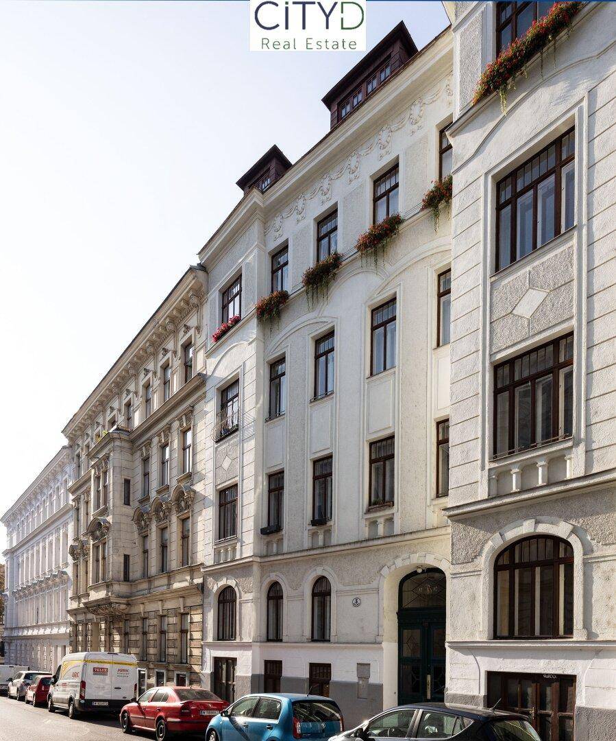Eindrucksvolle Fassade eines Altbaus mit vielen Fenstern und Blumenkästen an der Straße.
