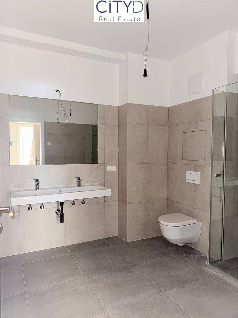 Modernes Badezimmer mit Doppelwaschbecken, wandhängendem WC und ebenerdiger Dusche.