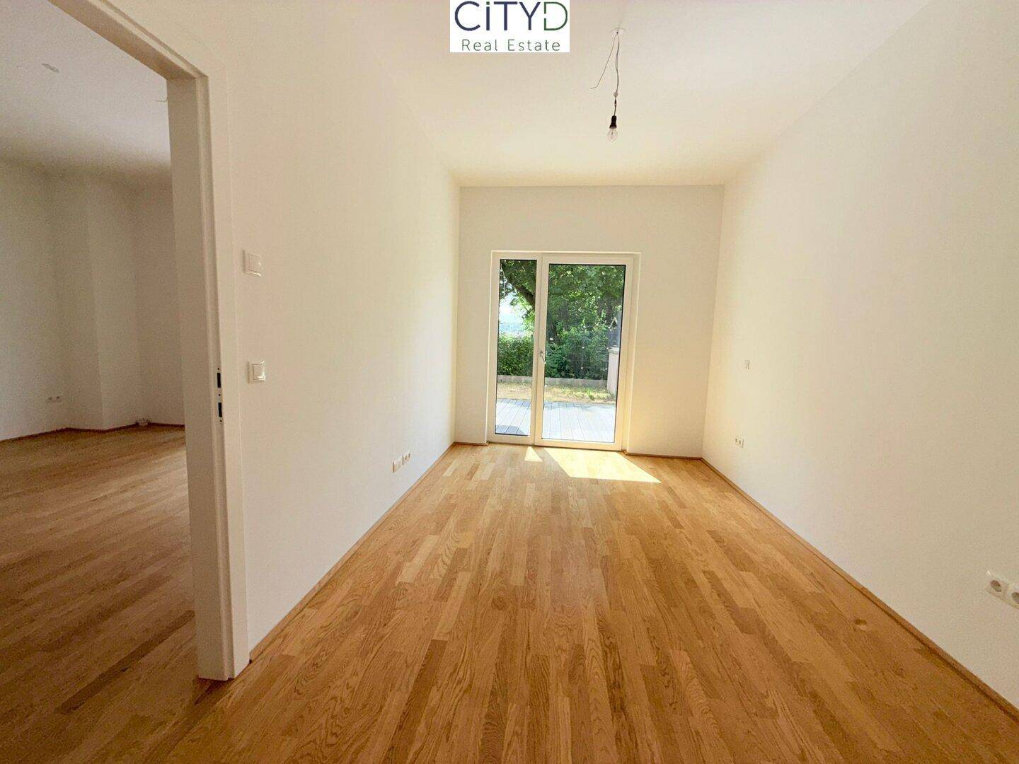 Helles Schlafzimmer mit Parkettboden und großem Fenster mit Zugang zum Außenbereich.