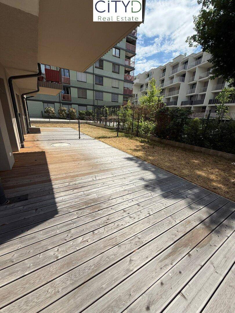 Holzterrasse mit angrenzender Rasenfläche und Blick auf umliegende Gebäude.