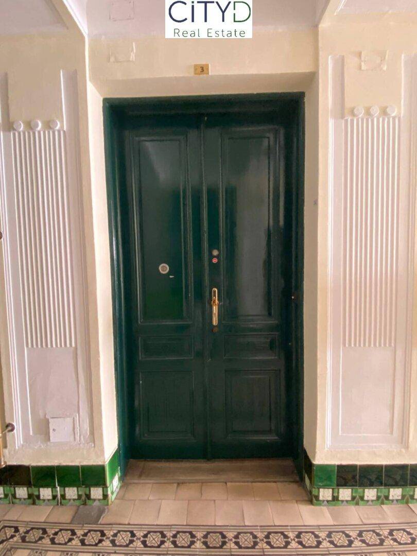 Ornate grüne Doppeltür mit dekorativen Wandpaneelen und gemustertem Fliesenboden im Eingangsbereich.
