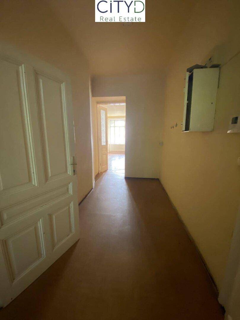 Heller Flur mit gelben Wänden, braunem Boden und Blick in einen weiteren Raum mit Fenster.