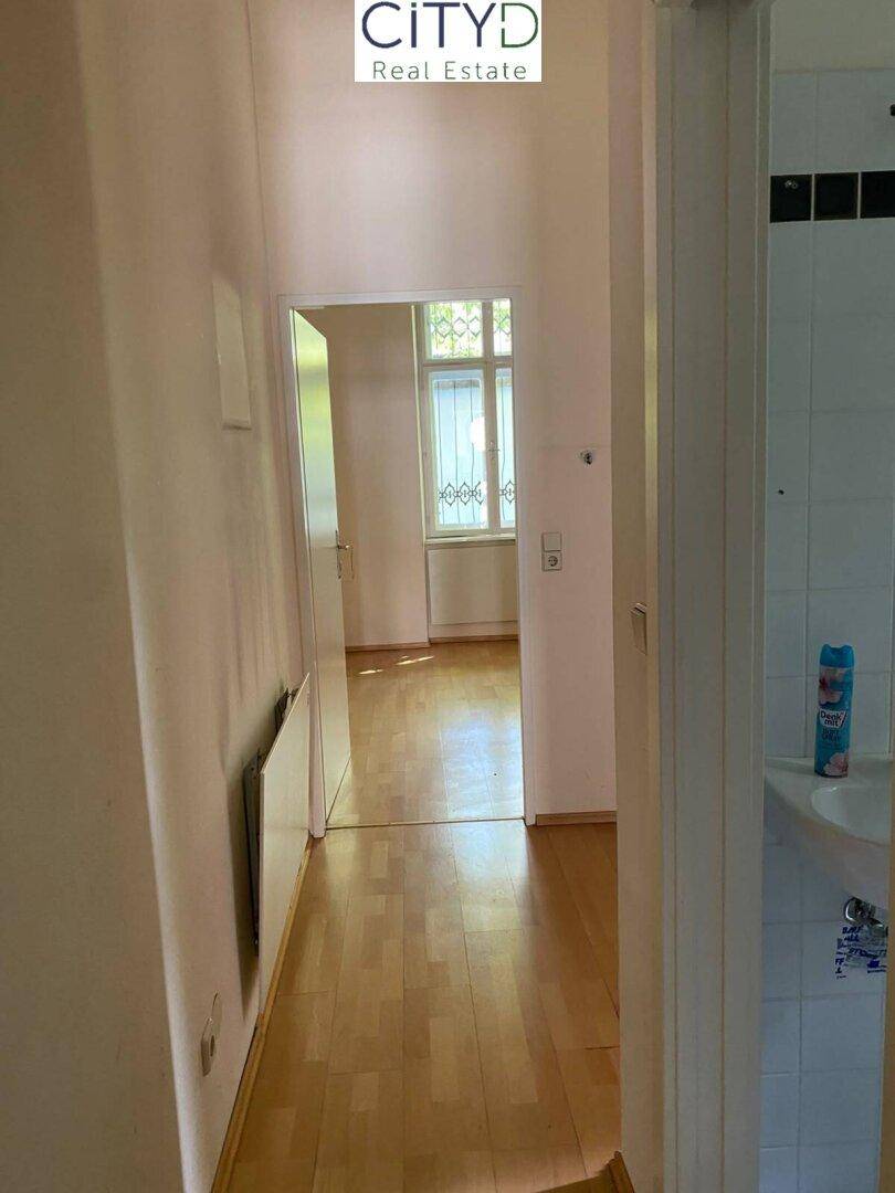Heller Flur mit Holzfußboden, Blick in ein Zimmer und angrenzendem Badezimmerbereich.