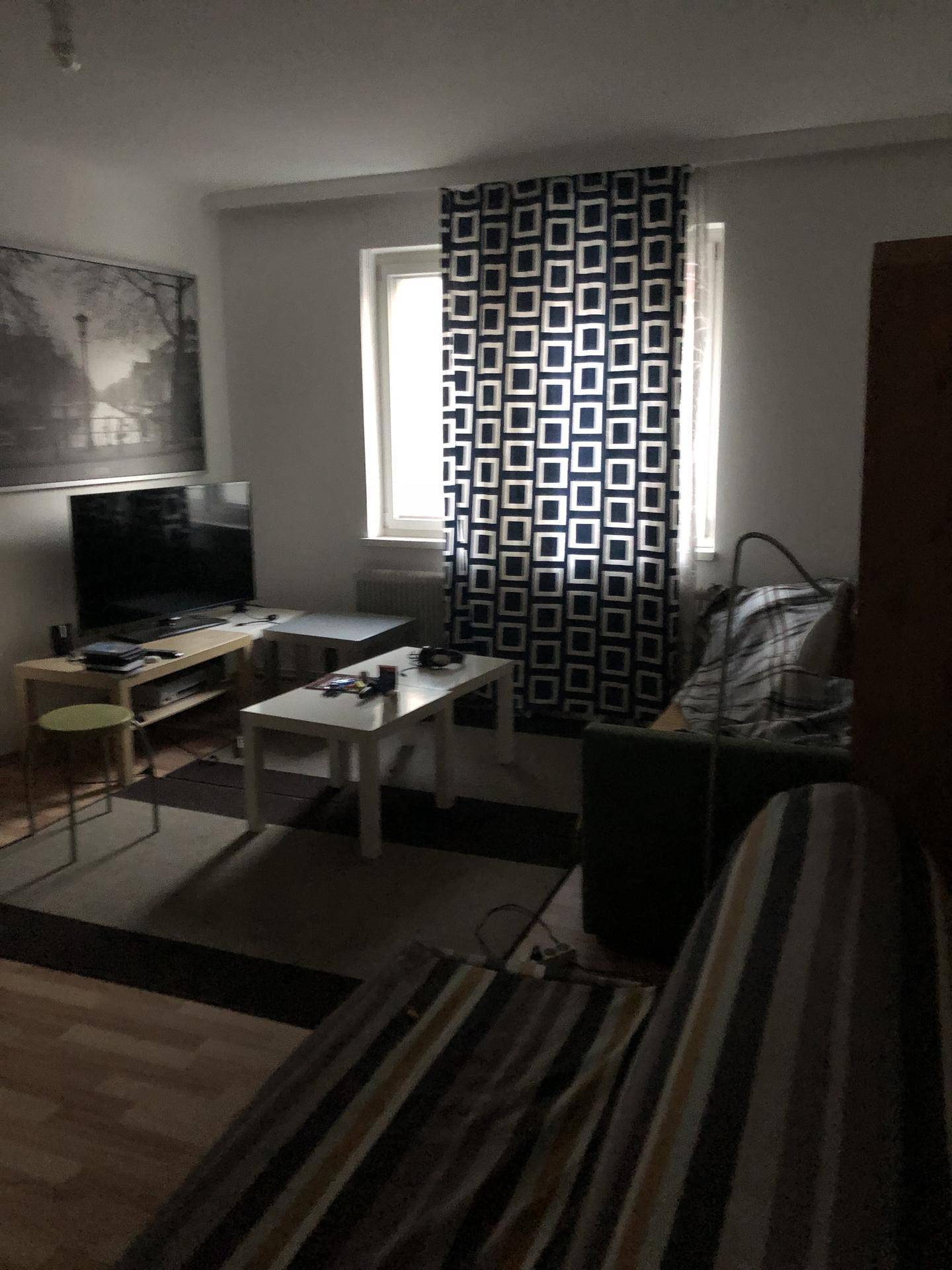Gemütliches Wohnzimmer mit Sofa, Fernseher und Couchtisch, beleuchtet durch ein Fenster.
