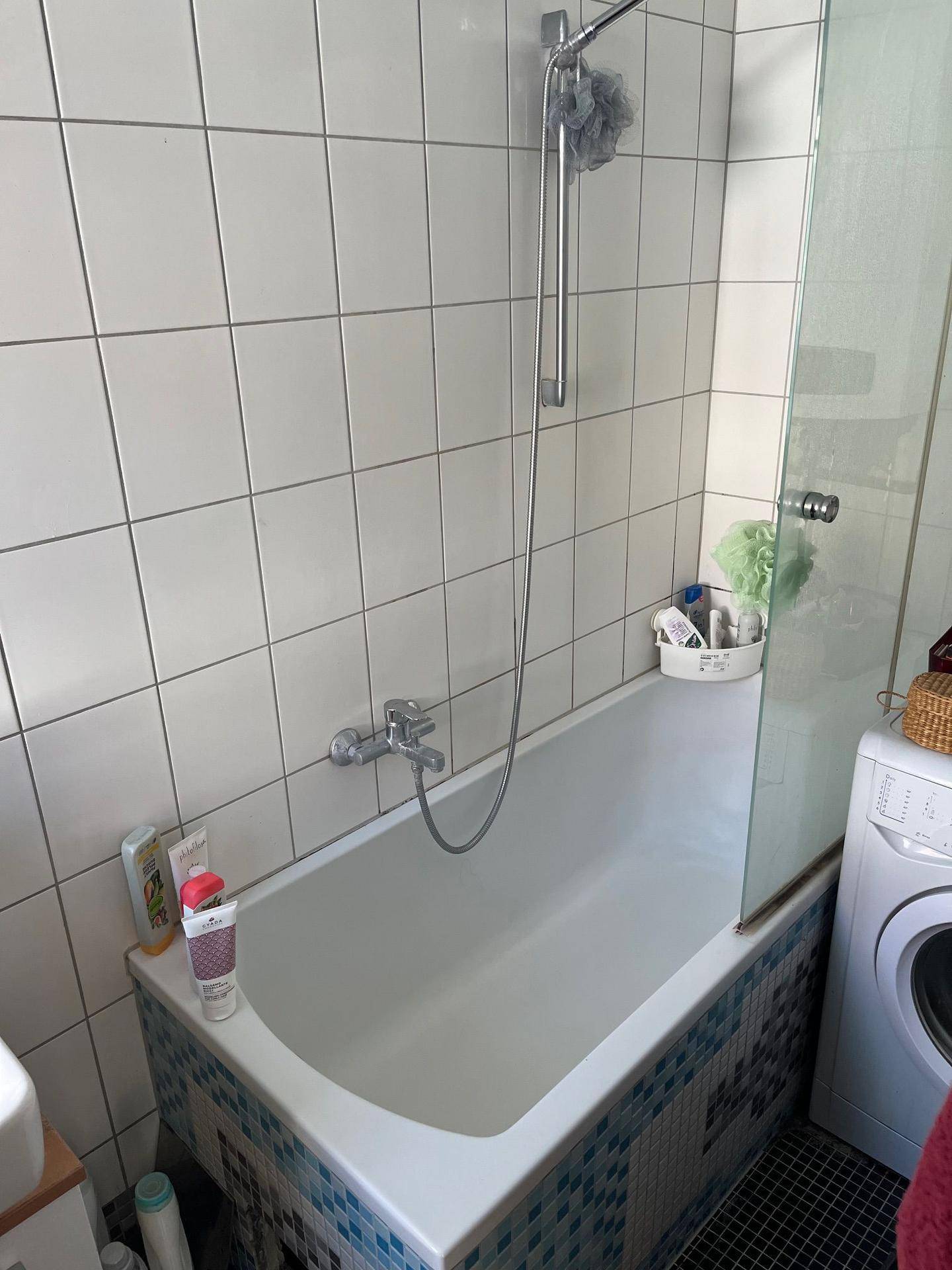 Badezimmer mit Badewanne, Duschabtrennung und Waschmaschine, gefliest.