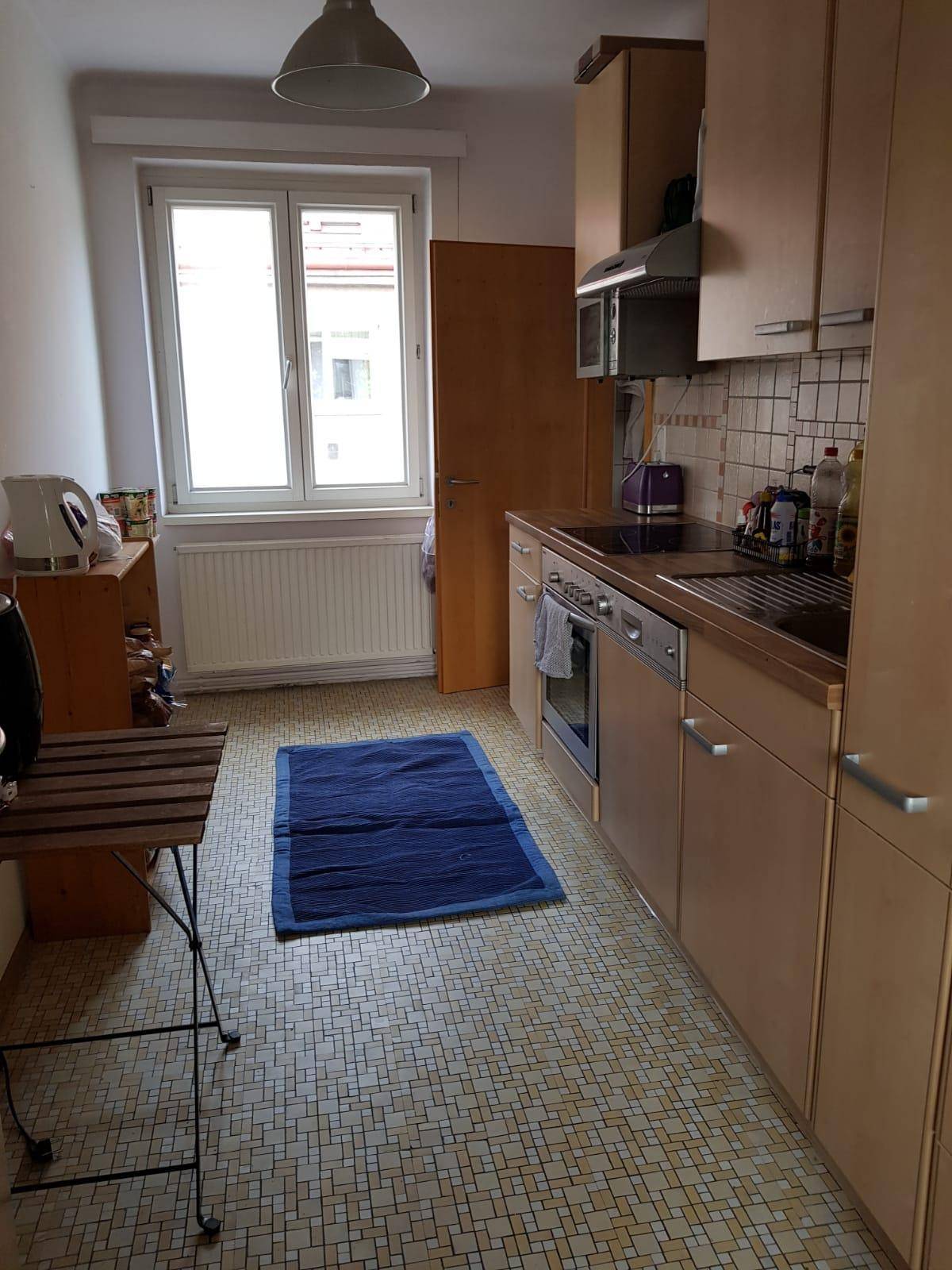 Funktionale Küche mit hellen Holzschränken, Fliesenboden und Fenster.