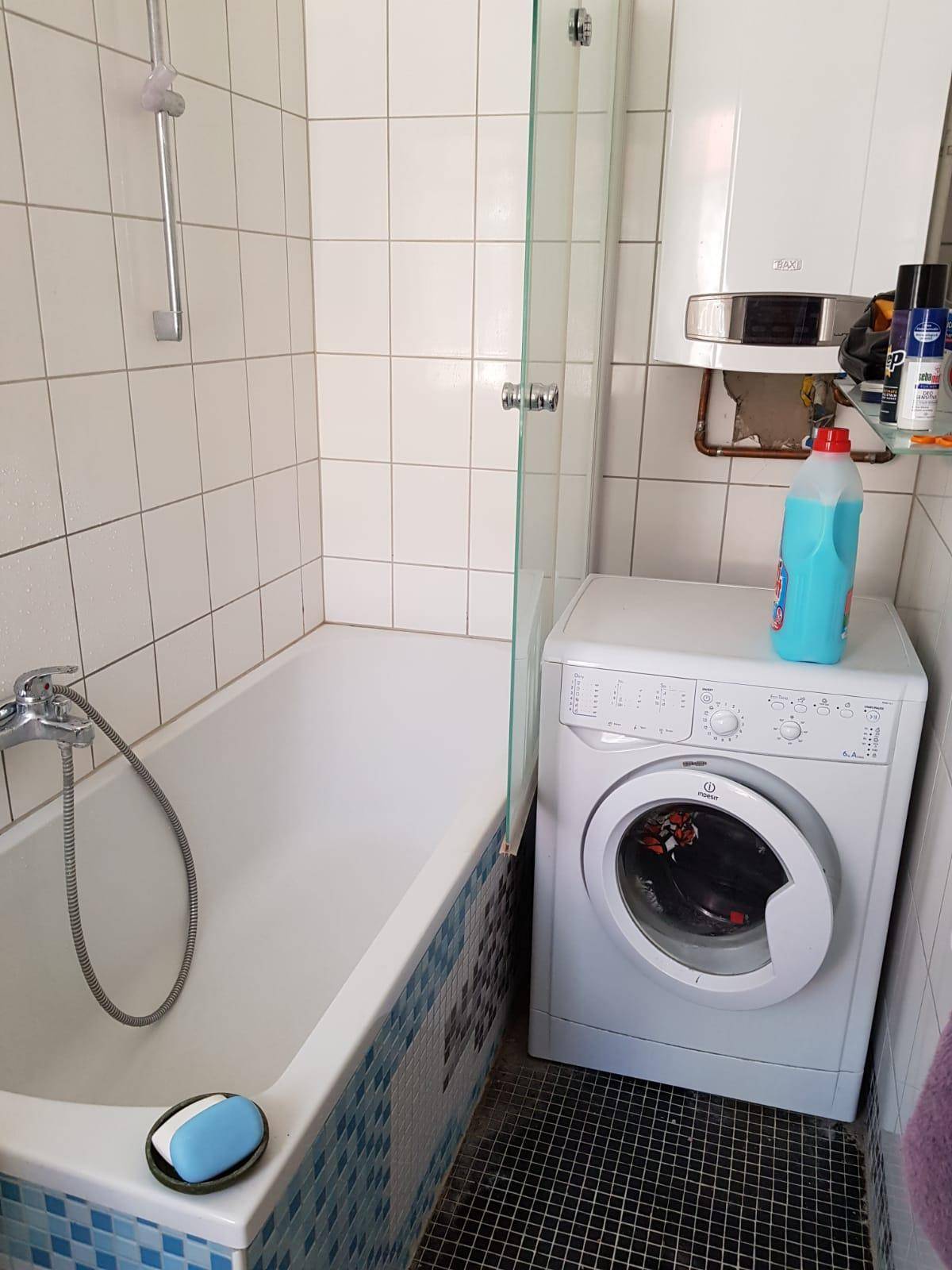 Badezimmer mit Badewanne, Duschabtrennung und Waschmaschine, gefliest.