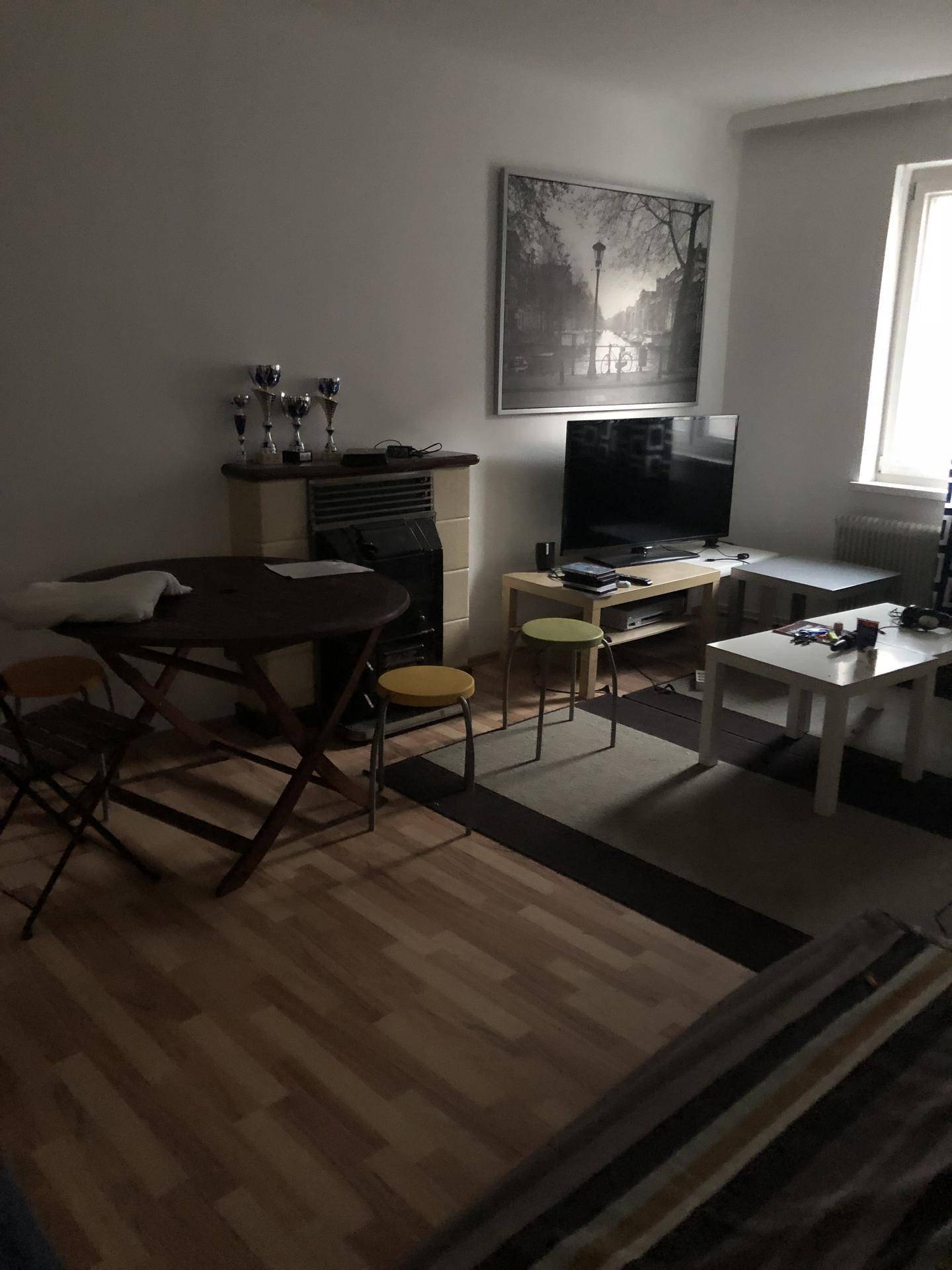 Wohnbereich mit Esstisch, Fernseher und einem Kachelofen, der Wärme spendet.