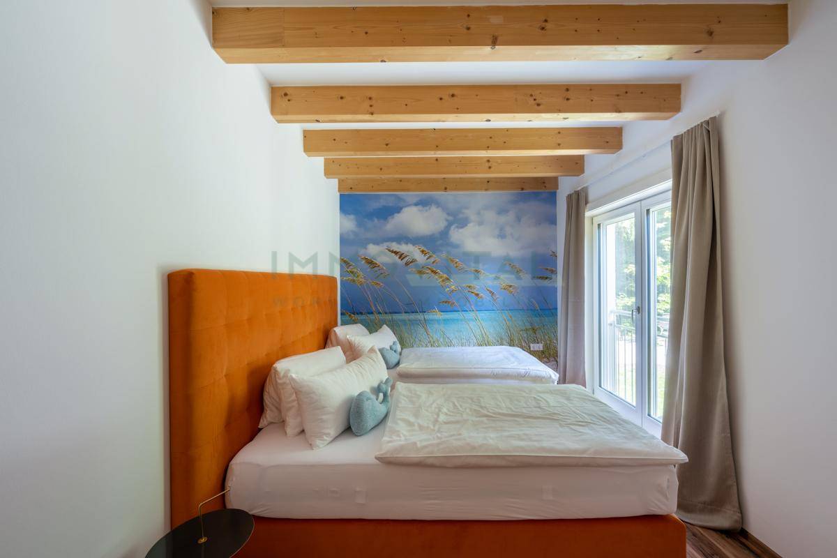 Helles Schlafzimmer mit freiliegenden Holzbalken, einer Wandtapete mit Strandmotiv und Zugang zum Balkon.