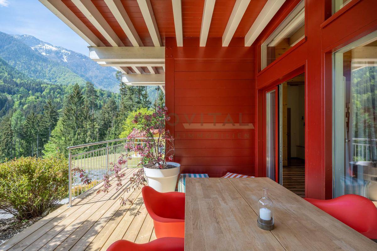 Sonniger Terrassenbereich mit Holztisch, roten Stühlen und weitem Bergblick.