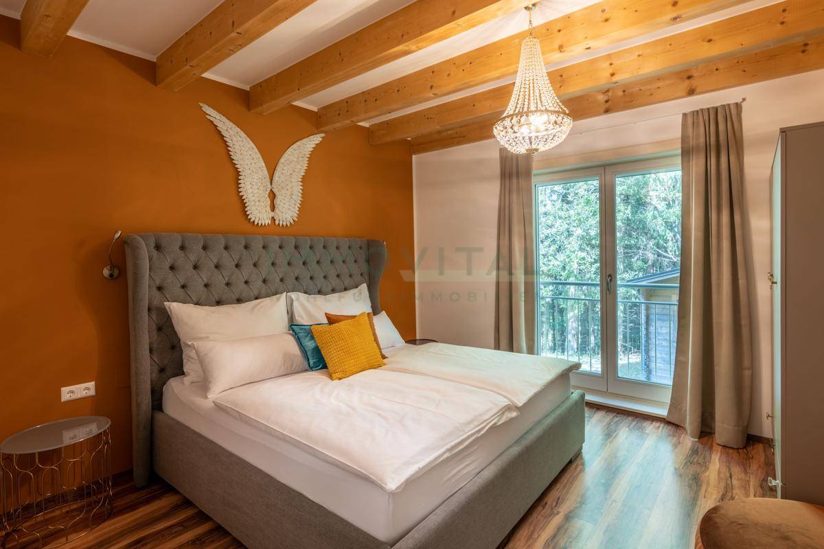 Schlafzimmer mit großem Bett, Holzbalkendecke und Zugang zu einem französischen Balkon.