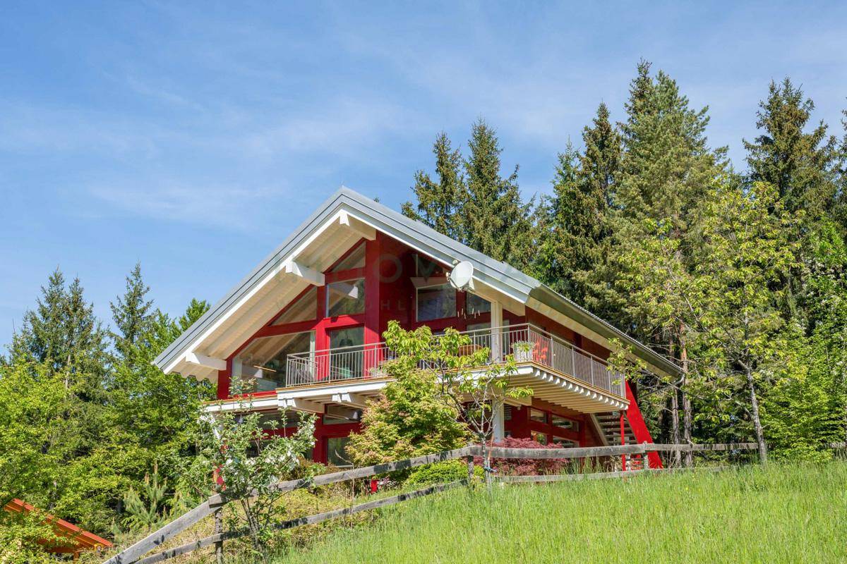 Freistehendes Holzhaus in idyllischer Berglandschaft mit viel Grün.