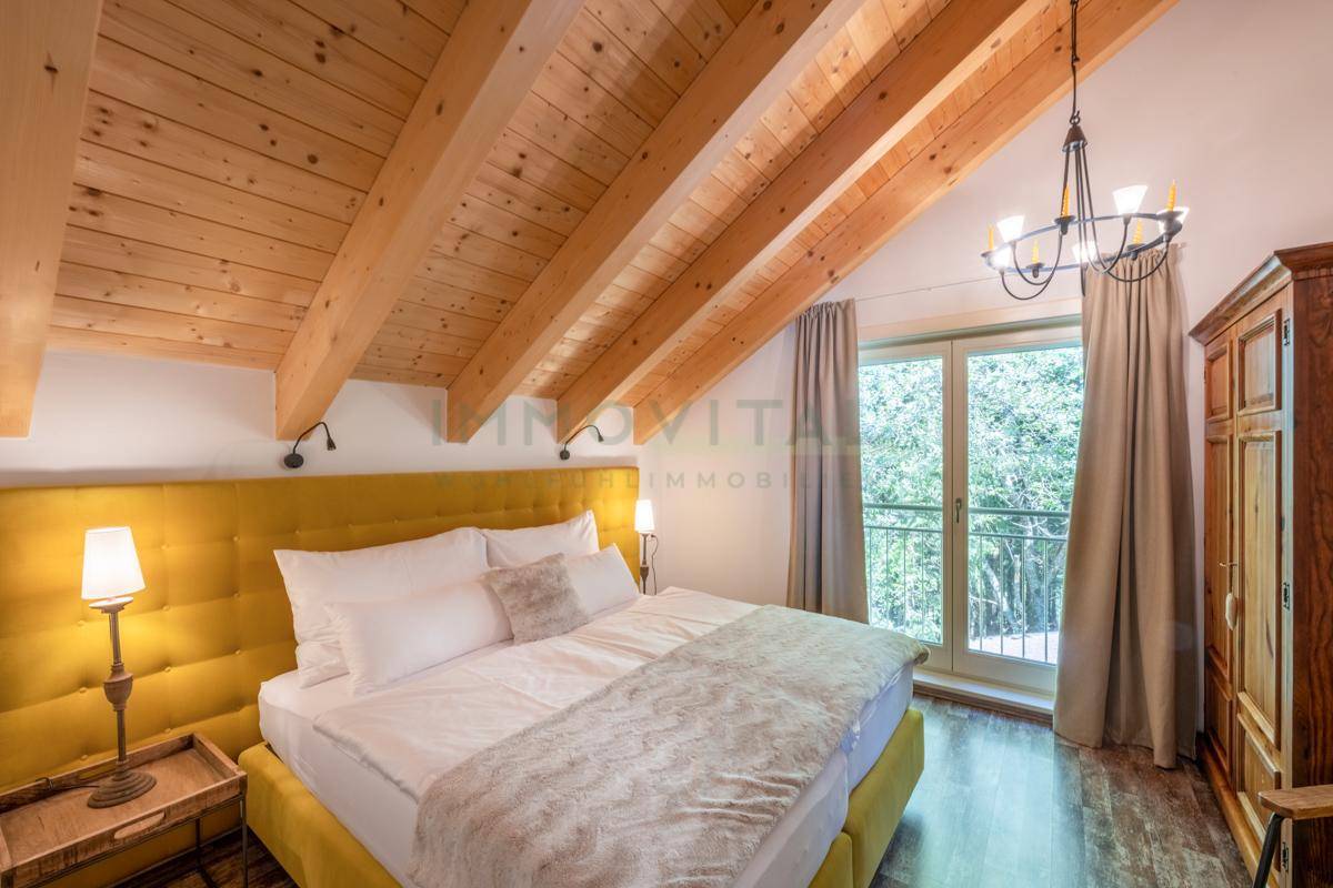 Gemütliches Schlafzimmer im Dachgeschoss mit Holzbalkendecke und Balkonzugang.