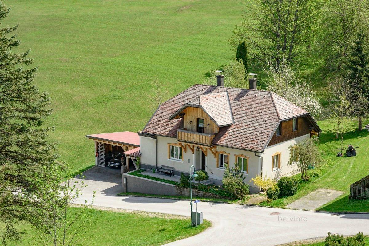 Malerisches Landhaus mit Carport, eingebettet in eine weite grüne Hügellandschaft.