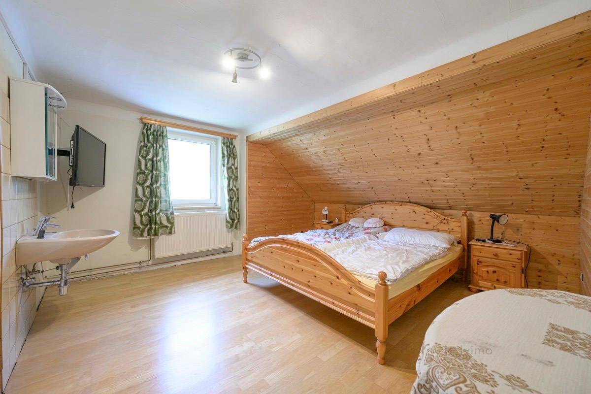 Gemütliches Schlafzimmer mit Holzverkleidung, Holzbett und kleinem Waschbecken.