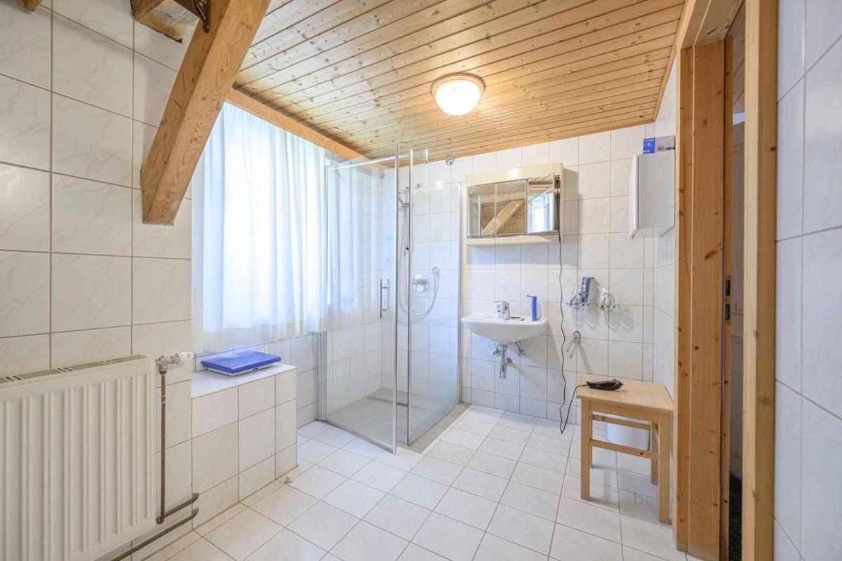 Helles Badezimmer mit Duschkabine, Waschbecken und Holzdecke im Dachgeschoss.