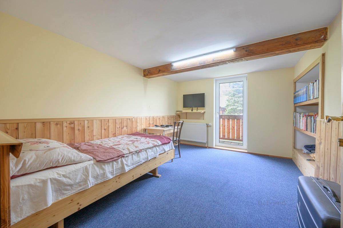 Helles Schlafzimmer mit Holzbalken, Teppichboden und Zugang zu einem kleinen Balkon.
