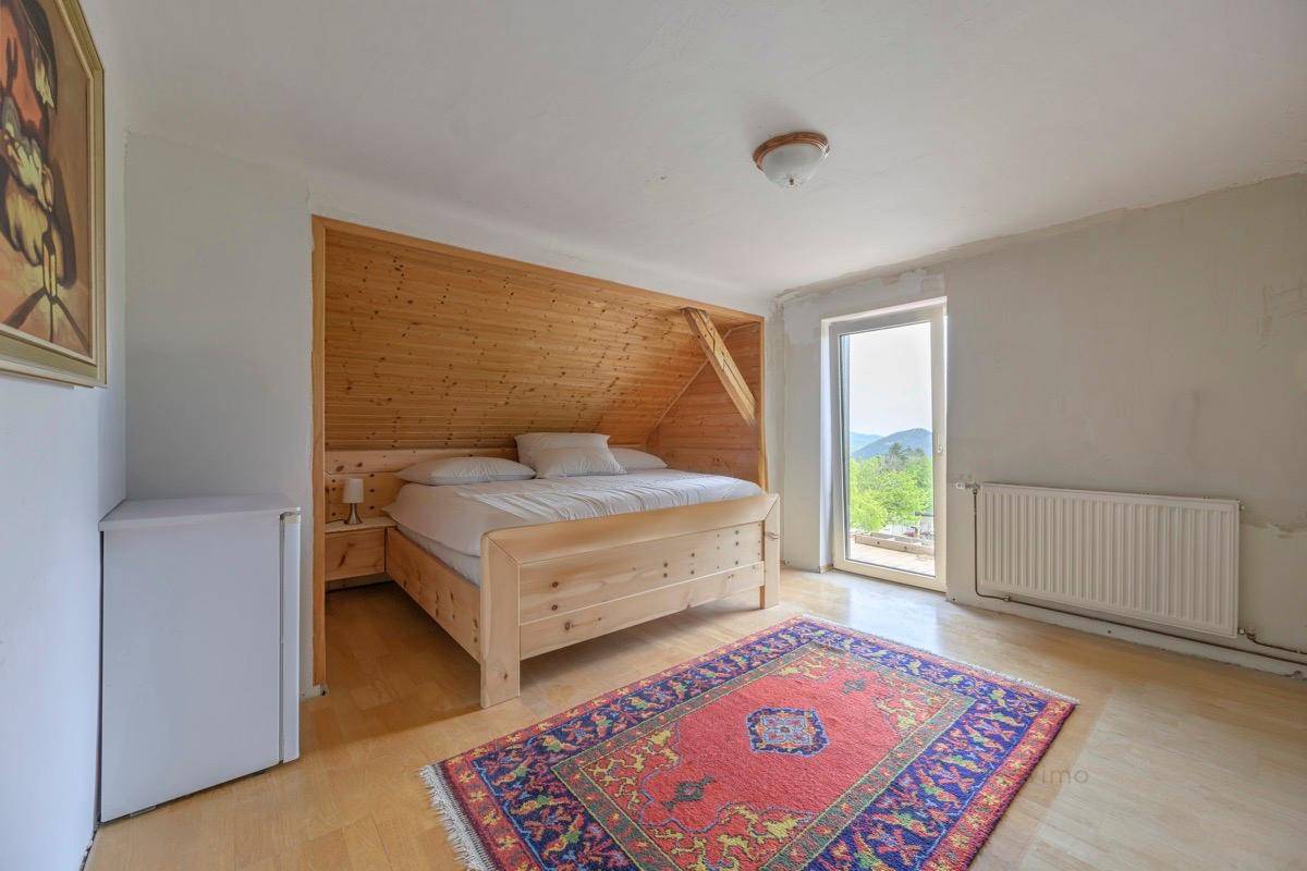 Schlafzimmer im Dachgeschoss mit Holzbett, Teppich und Zugang zu einem Balkon mit Bergblick.