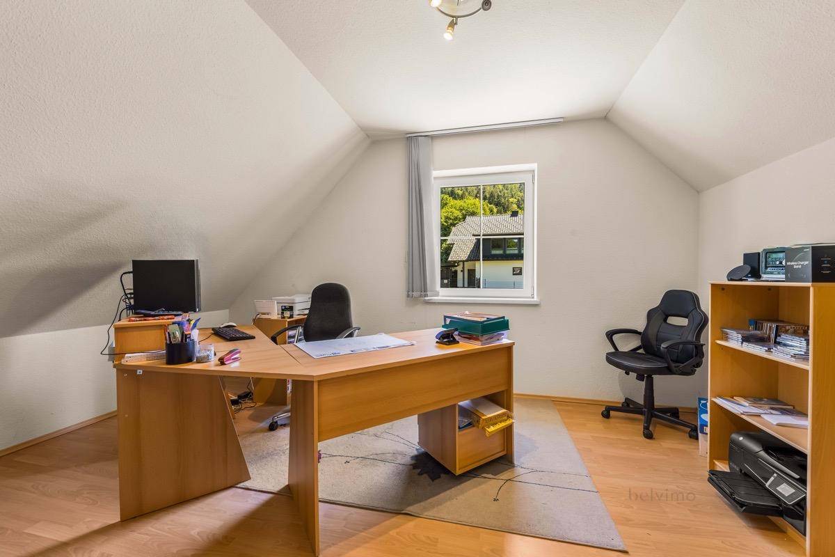 Helles Arbeitszimmer im Dachgeschoss mit Schreibtisch, Holzmöbeln und schräger Decke.